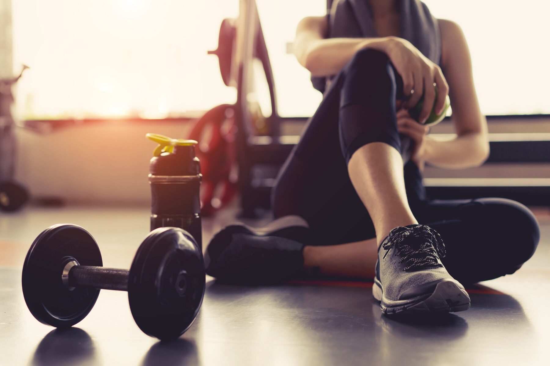 Woman in a gym sitting on the floor with a weight and a water bottle